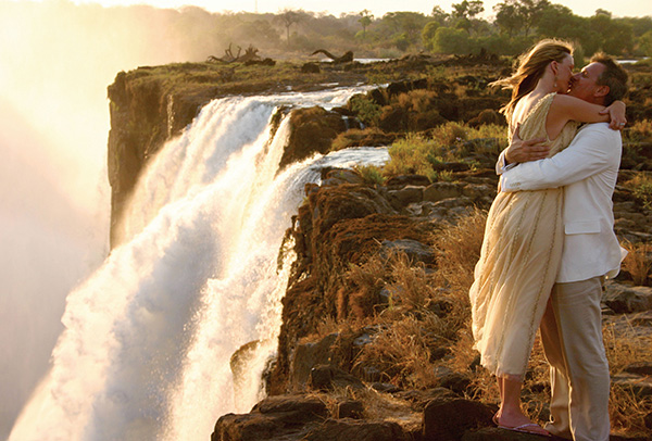 Couple embracing on the edge of Victoria Falls at Livingstone Island, Zambia
