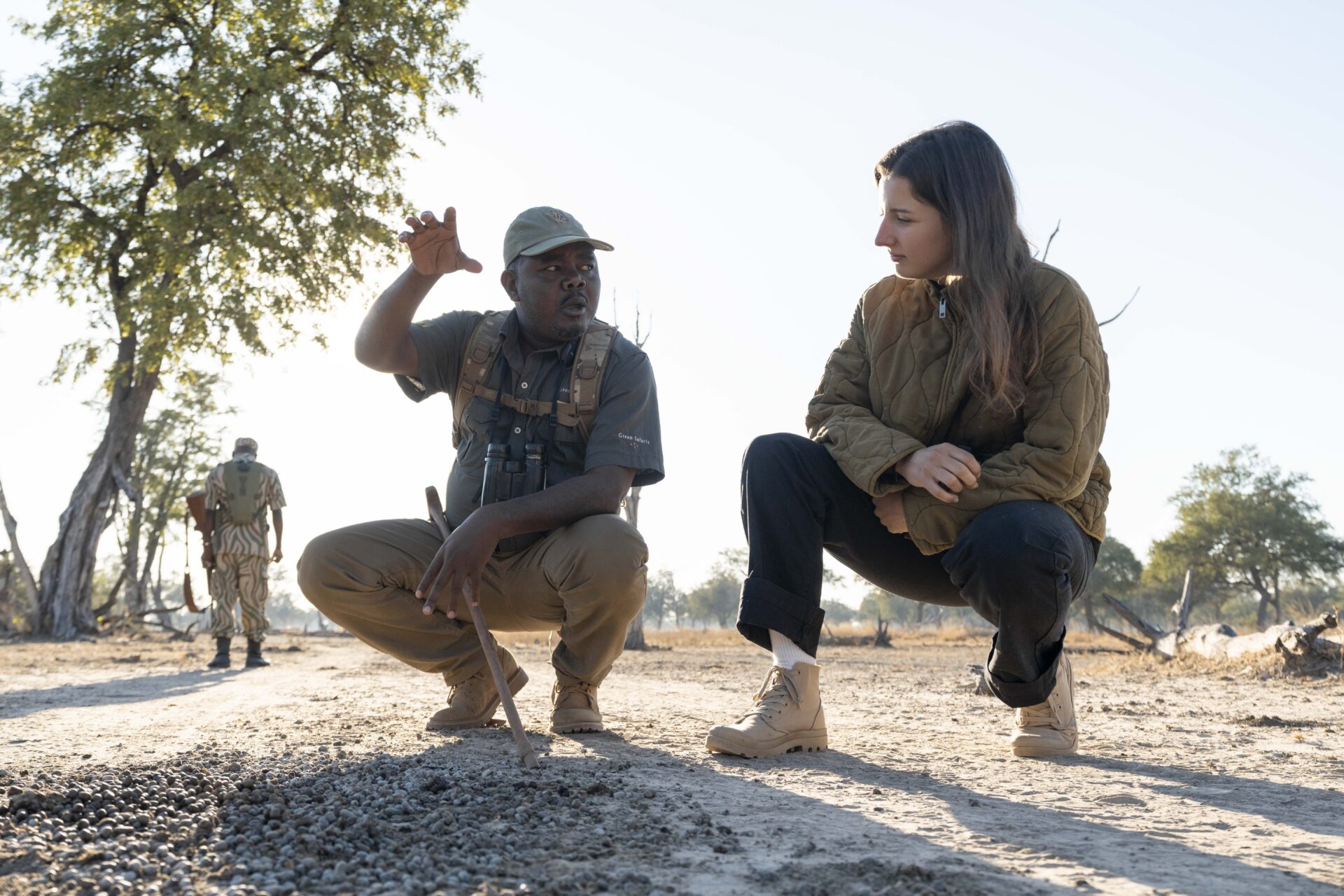 Shawa Luangwa Camp guide crouching to explain animal tracks to a guest on a walking safari in South Luangwa